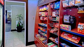 A snack aisle with various chips and snacks, a Coca-Cola sign, and a potted plant. - Equipped Suite Near CHA | Indoor Pool + Gym Access (Chattanooga)