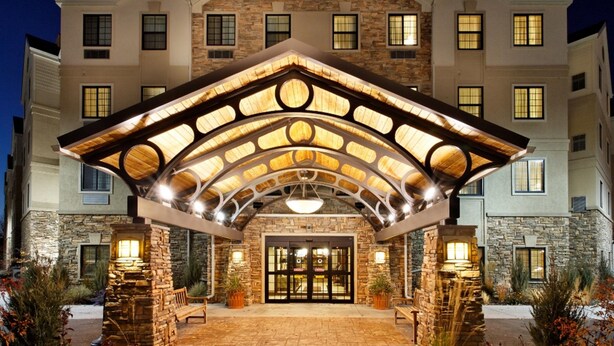 A Staybridge Suites hotel with a stone facade, large entrance, and a covered patio area. - Studio Suite | Indoor Pool, Hot Tub, Free Wi-Fi (Dearborn)