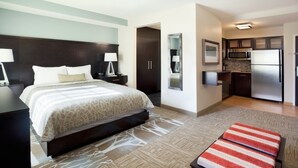 A hotel room with a bed, bedside tables, a mirror, a kitchenette, and a small seating area. - Studio Suite | Indoor Pool, Hot Tub, Free Wi-Fi (Dearborn)