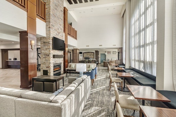 A spacious hotel lobby with a fireplace, seating areas, and large windows.