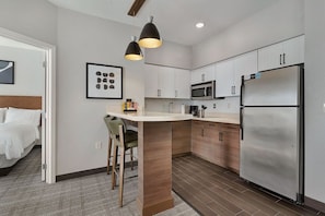 A modern kitchen with white cabinets, a stainless steel refrigerator, a microwave, and a bar stool.