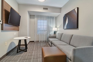 A hotel room with a sofa, a small table, a TV, and a painting on the wall.
