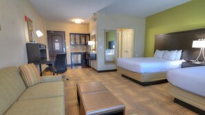 Ein Hotelzimmer mit Sofa, Bett, kleinem Tisch, einer Küchenzeile und einem Badezimmer.