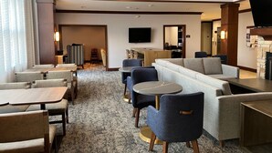 A hotel lobby with a seating area, a flat-screen TV, a fireplace, and a staircase.