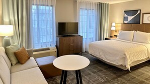A hotel room with a bed, a TV, a sofa, a small table, and a desk with a lamp.