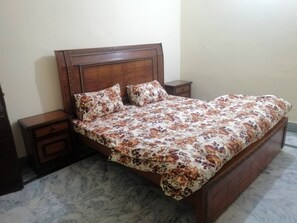 A bed with a floral bedspread, wooden headboard, and two nightstands with drawers. - Remarkable 3-bedroom (Gujar Khan)