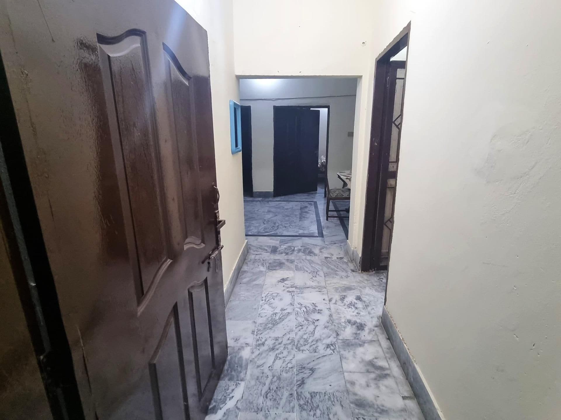 A hallway with a marble floor leading to a room with a bed and a chair.