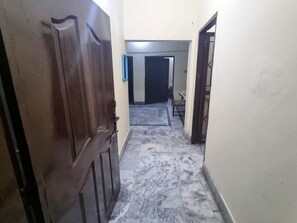 A hallway with a marble floor leading to a room with a bed and a chair. - Remarkable 3-bedroom (Gujar Khan)