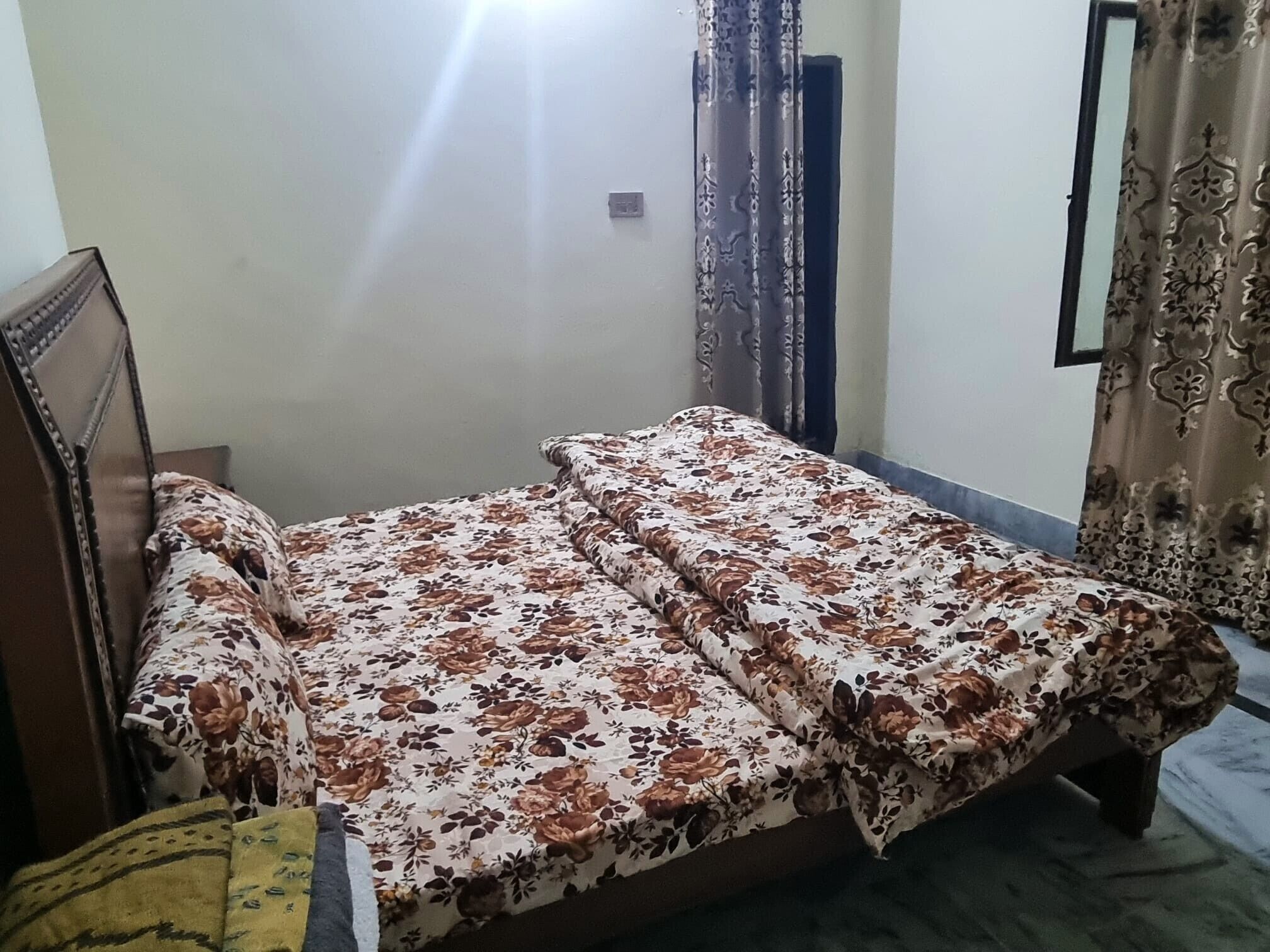 A single bed with a floral bedspread in a room with a plain wall and a door.