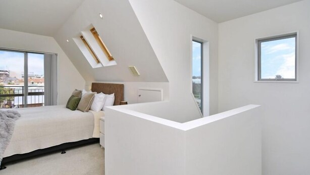 A modern bedroom with a sloped ceiling, a bed with pillows, a nightstand, and a window.