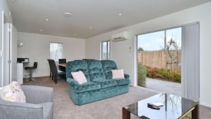 A living room with a teal sofa, a grey armchair, a glass coffee table, and a dining area with a table and chairs.