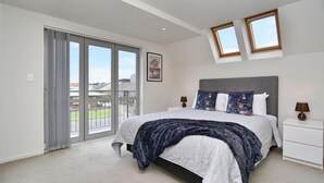 A bedroom with a large bed, a nightstand, two bedside lamps, a window, and a view of the outside.