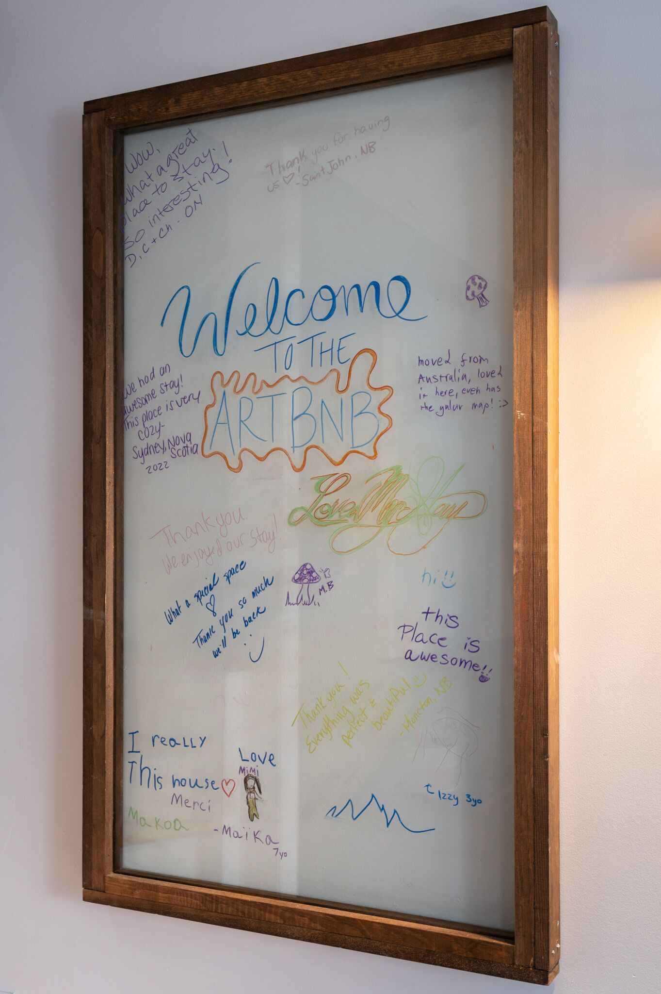 Una lavagna con il messaggio 'Welcome to the ARTBNB' circondata da appunti e disegni colorati scritti a mano.