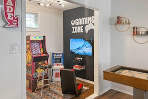 Una sala de juegos con máquinas de arcade, mesa de billar y una gran pantalla de televisión.