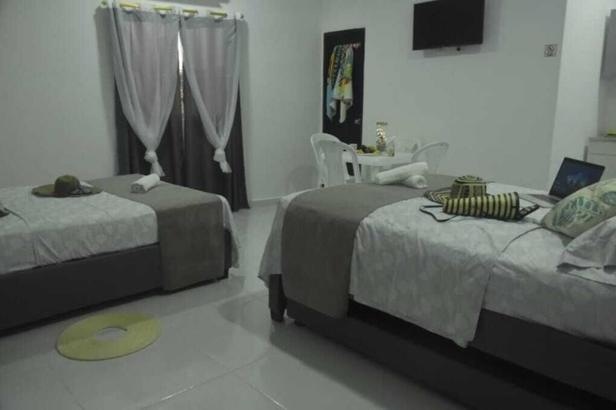 A hotel room with two single beds, a small table with a laptop, a TV on the wall, and a curtain.