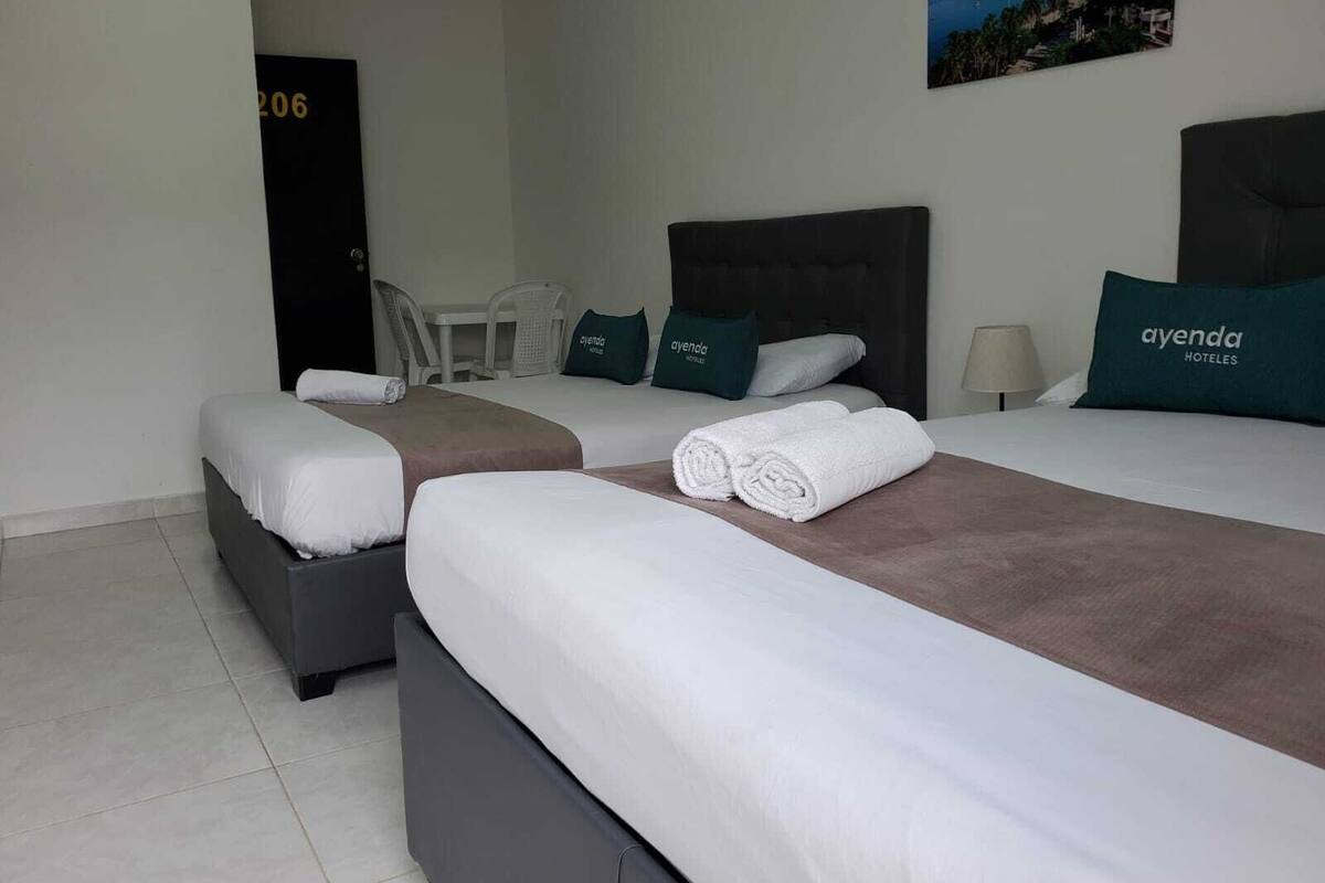 A hotel room with two beds, a desk, and a chair. There are towels on the beds and a picture on the wall.