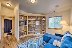 Un salon chaleureux avec un canapé bleu, une bibliothèque en bois et une fenêtre équipée de stores.