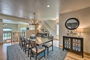 Un espace repas comprenant une table à plateau en verre, des chaises en bois, un lustre et un escalier menant à un autre niveau.