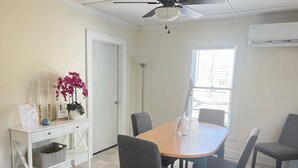 A dining area with a table, chairs, a ceiling fan, a window with blinds, and a white door.