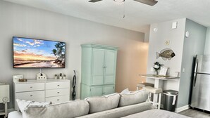 Une chambre à coucher comprenant un lit, une commode, une coiffeuse, un ventilateur de plafond et un téléviseur fixé au mur.