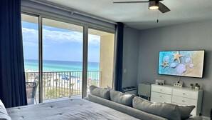 Une chambre d’hôtel dotée d’un grand lit, d’un coin salon, d’une télévision à écran plat et d’un balcon offrant une vue sur la plage et l’océan.