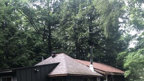 A cabin with a wooden deck and a small porch, surrounded by dense forest. - Lake Front Cottage Property  (Bracebridge)