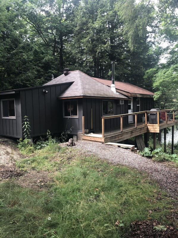 A cabin with a wooden deck and a small porch, surrounded by dense forest.