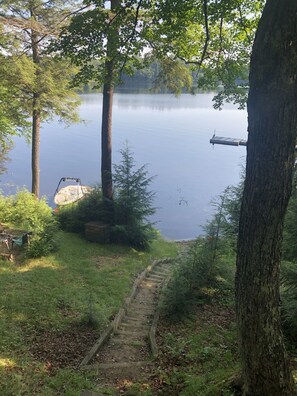 A wooden staircase leading to a dock by a calm lake, surrounded by trees and greenery.