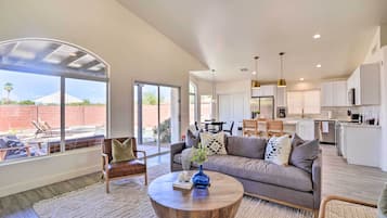 A spacious living area with a large window, a sofa, a coffee table, and a kitchen in the background.