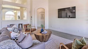 Een moderne woonkamer met een hoekbank, een ronde salontafel en een flatscreen tv aan de muur.