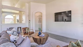 A modern living room with a sectional sofa, a round coffee table, and a flat-screen TV mounted on the wall.