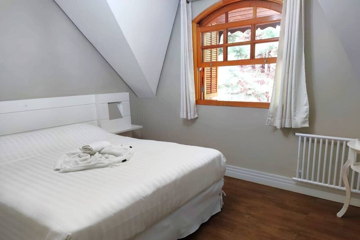 Une chambre à coucher avec un lit, une table de chevet, une fenêtre avec des rideaux et un radiateur.