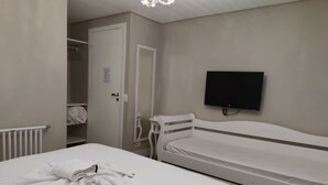 Een slaapkamer met twee eenpersoonsbedden, een witte kledingkast, een aan de muur bevestigde televisie en een deur naar een badkamer.