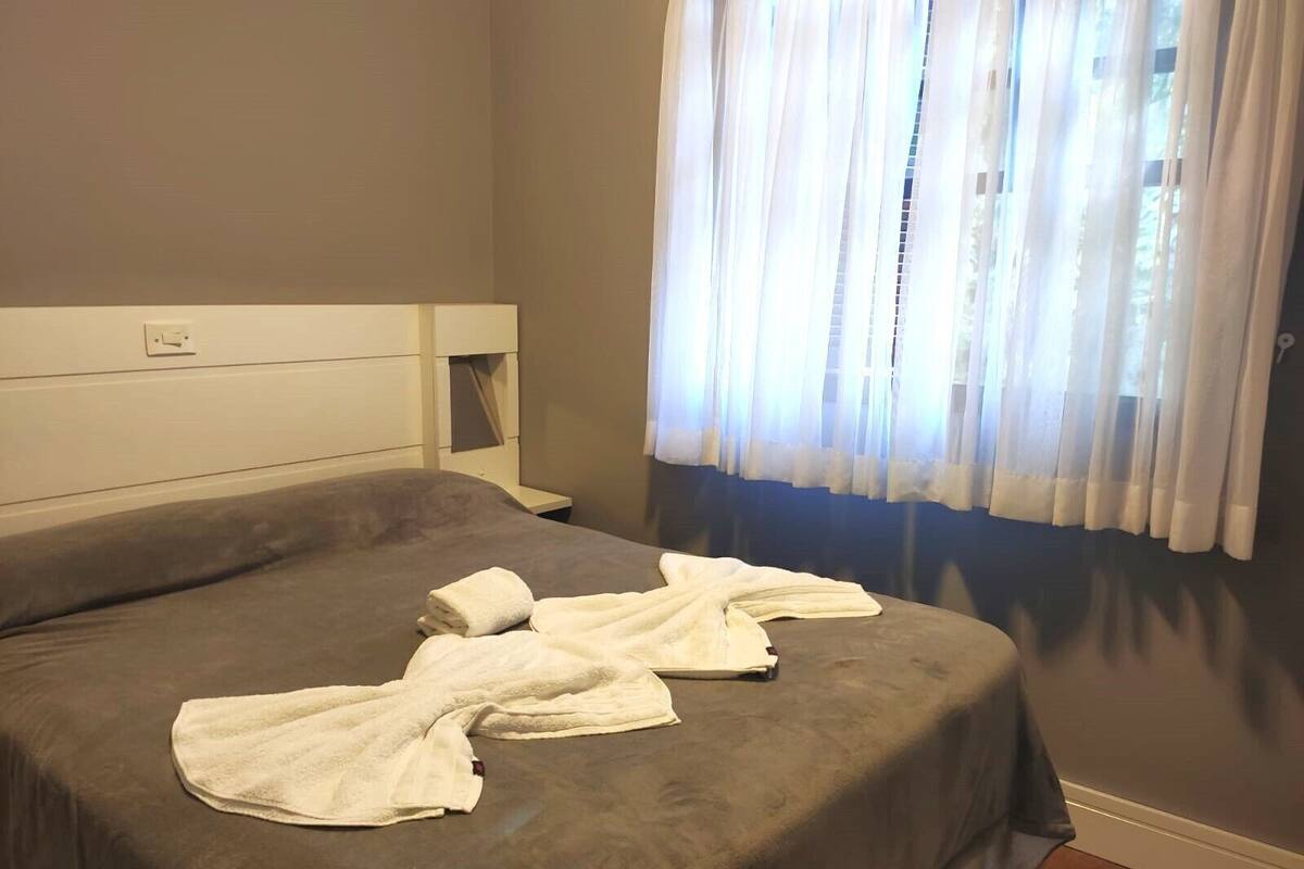 Une chambre d’hôtel avec un lit, une table de chevet, une prise de courant et des rideaux en voile.