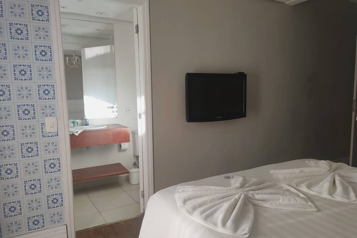 Une chambre d’hôtel avec un lit, un téléviseur fixé au mur, une salle de bain avec un miroir et une porte à motifs.