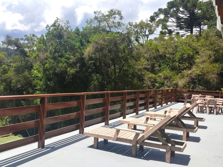 Una terraza de madera con bancos y mesas, rodeada de baranda de madera, con vistas a un paisaje verde y exuberante.