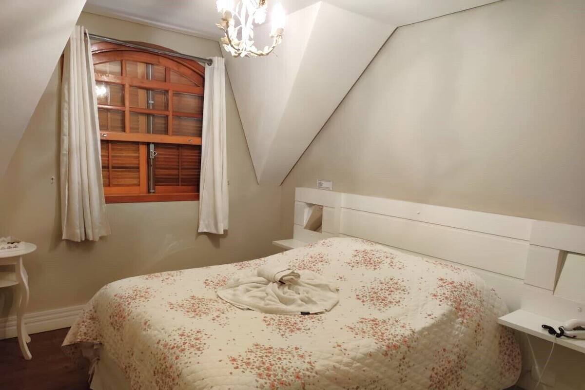 Une chambre à coucher avec un lit, une fenêtre avec des rideaux, une petite table et un lustre.