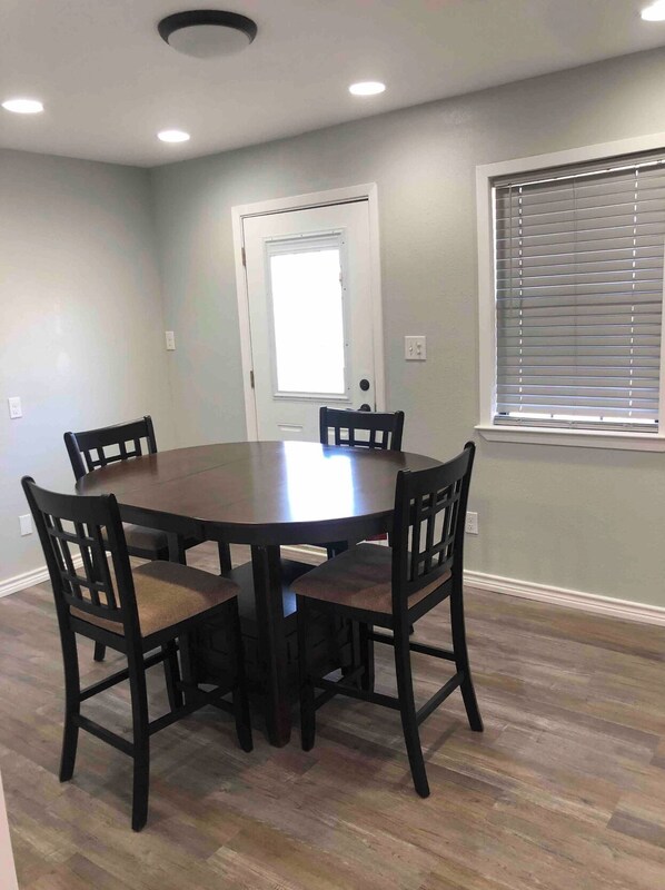 A dining area with a round table and four chairs, a door, and a window with blinds.
