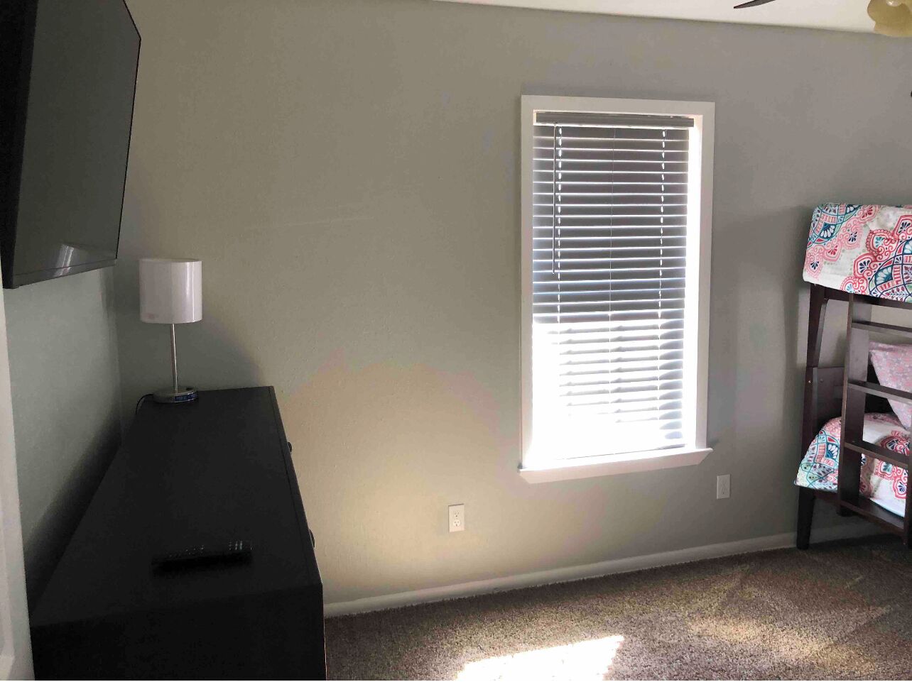 Ein Zimmer mit Fenster, Schreibtisch mit Lampe und Etagenbett mit gemusterten Betttextilien.