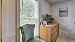 Een kamer met een stoel, een rieten dressoir, een televisie en een lijst met een foto aan de muur.