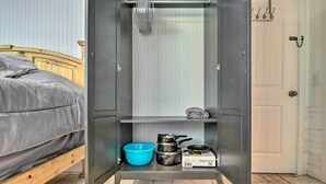 Een compacte kamer met een bed, een kitchenette met pannen, een blauwe kom en een kookplaat.