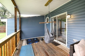 A covered outdoor deck with a hammock, two exercise mats, and a wooden railing.