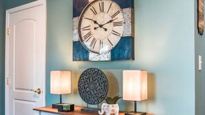 Un couloir avec une console blanche, deux lampes fixées au mur, une horloge décorative et une porte.