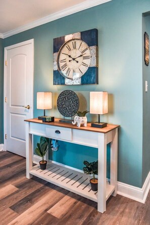 Un pasillo con una consola blanca, dos lámparas de pared, un reloj decorativo y una puerta.
