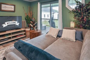 Una sala de estar con un sofá, un televisor y una ventana con vista a una terraza.