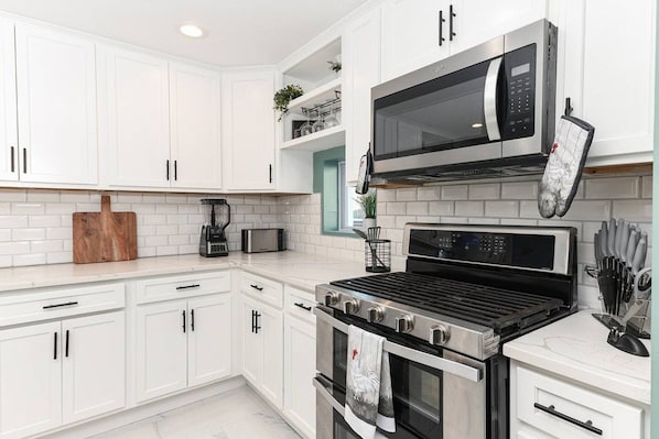 A modern kitchen with white cabinetry, a built-in oven, a microwave, and a coffee maker.