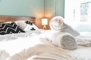 Un lit bien fait, avec une serviette blanche roulée, un oreiller noir et blanc et une lampe de chevet.