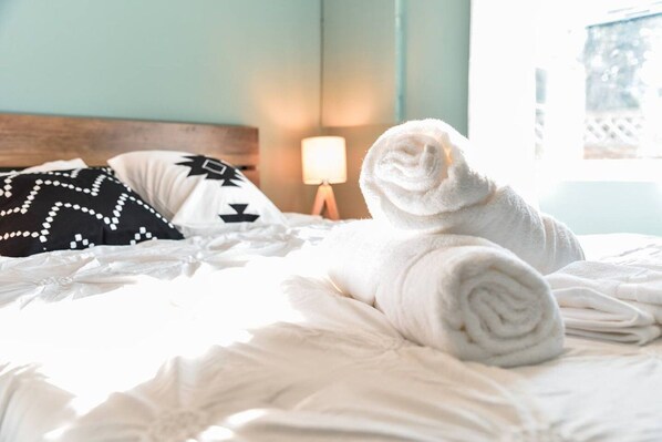 A neatly made bed with a rolled white towel, a black and white pillow, and a bedside lamp.