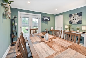 A dining room with a long wooden table, chairs, and a 'WELCOME' sign on the wall.