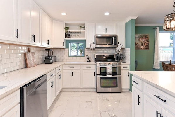 A modern kitchen with white cabinets, stainless steel appliances, and a window providing natural light.